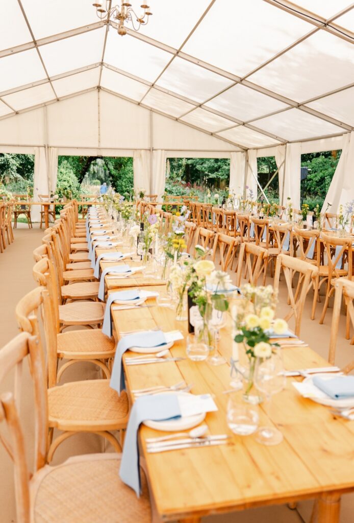 Long tables dressed wiith bud vases filled with soft blue, lemon, cream and white natural flowers at Chaucer Barn wedding venue Norfolk 