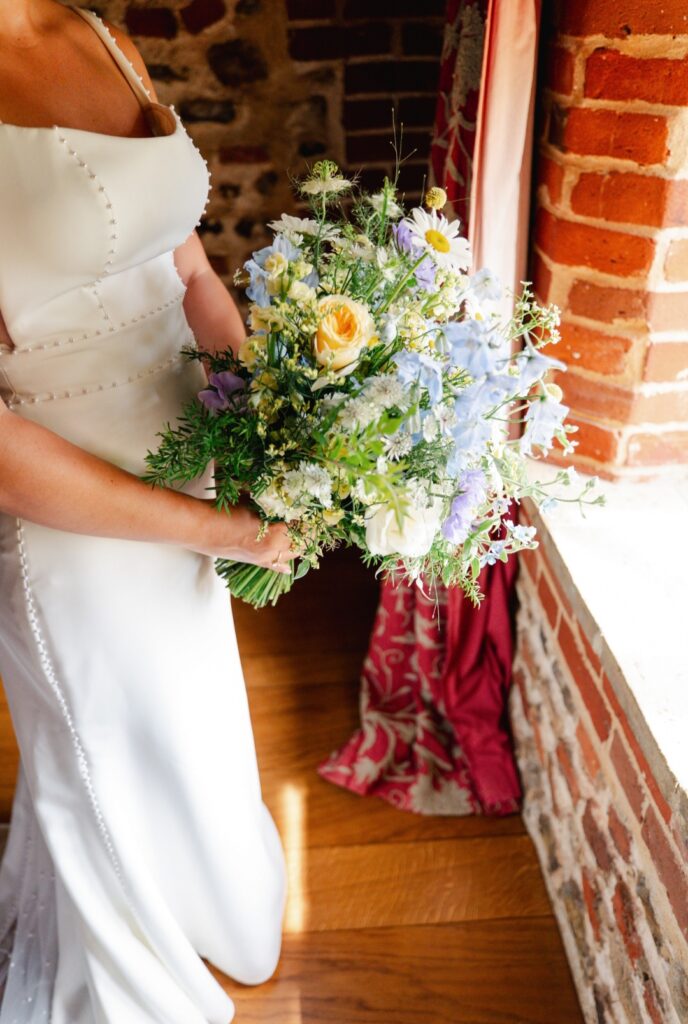 Natural meadow style bridal bouquet for Emily in shades of lemon, soft blue and white at Chaucer Barn wedding venue in Norfolk