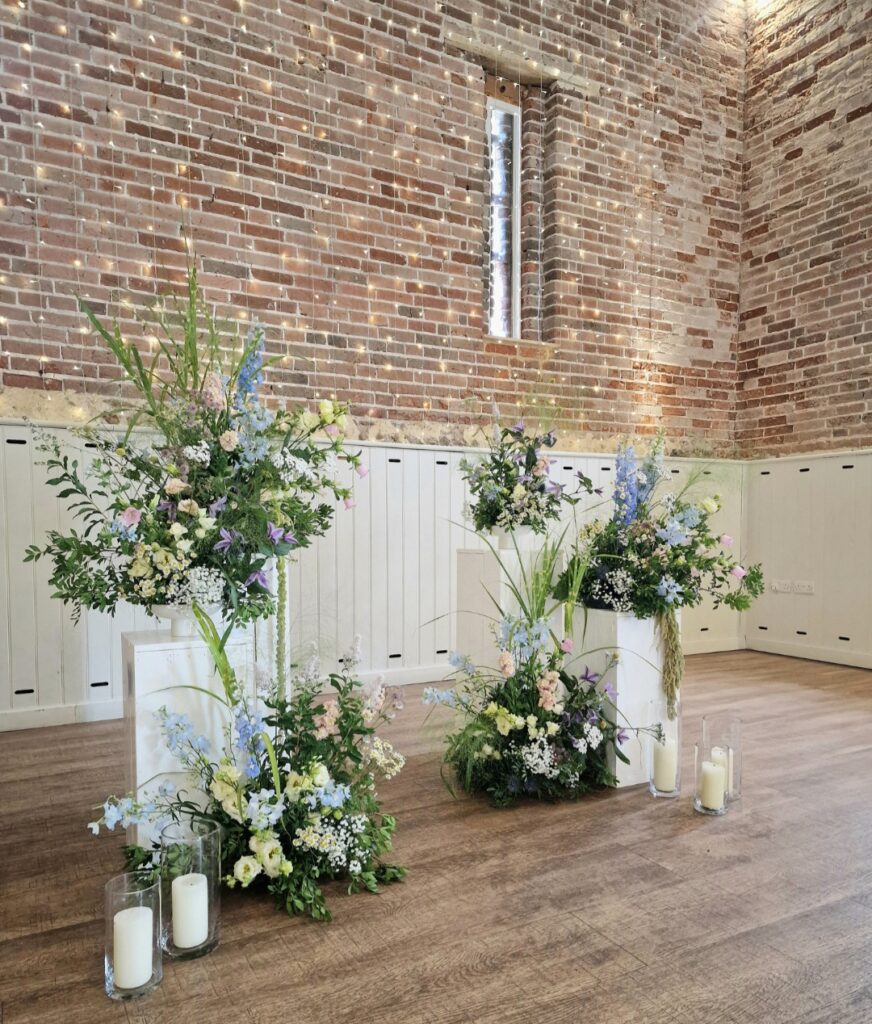 Natural meadow ceremony flowers upon columns at different levels and finished with church candles in glass vases